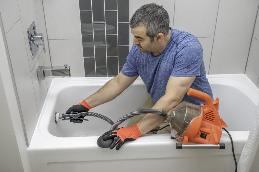 Man using a mini plumbers snake to unclog a bathtub drain