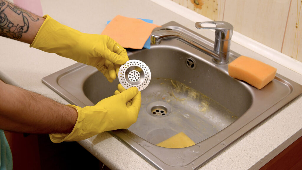 Cleaner in rubber gloves shows clean plughole protector of a kitchen sink