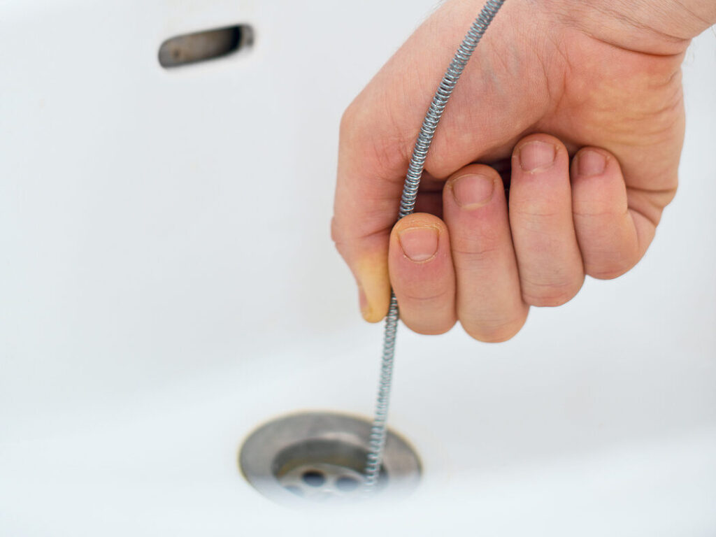 Plumber repairing sink with a plumber's snake.